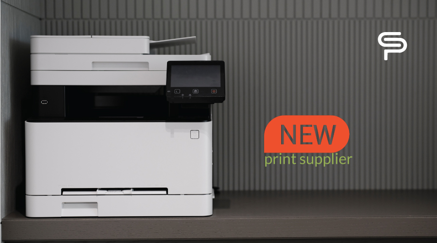 Office multifunction printer next to a sign reading New print supplier